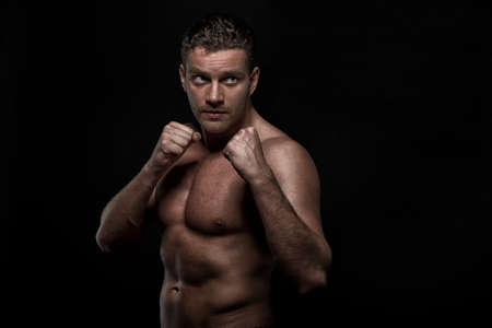 Ready to fight. Portrait of serious handsome young shirtless man looking at camera while standing against black backgroundの写真素材