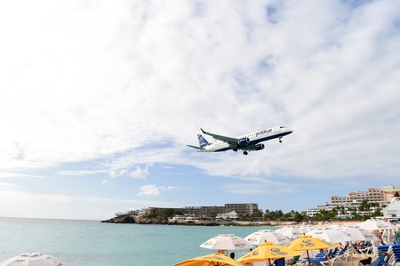 ST. MAARTEN, ANTILLES, Netherlands - January 24, 2016: JetBlue plane lands on Juliana International Airport in Netherlands Antilles above water and beach with umbrellasのeditorial素材
