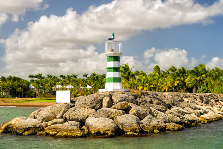 beautiful lighthouse with stripes on stony harbour near water sunny day outdoor with green palm trees and cloudy blue sky at summerの写真素材