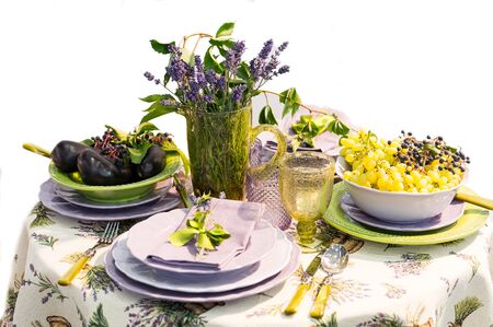 table serve floral decoration yellow green and violet colors with eggplant grapes flowers in vase plates fork spoon and knife isolated on white backgroundの写真素材