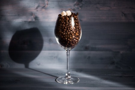 Roasted coffee beans and sugar cubes inside wine glass on vintage wooden background. Side viewの写真素材