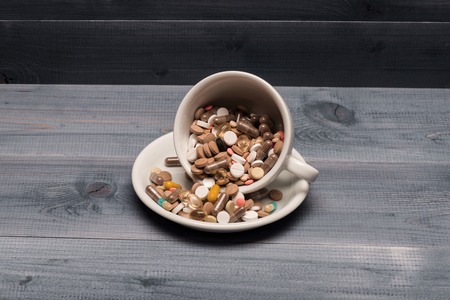 Medical capsules and tablets inside coffee cup on vintage wooden background. Side viewの写真素材