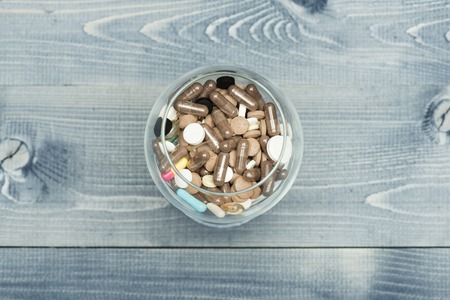 Medical capsules and tablets inside glass on vintage wooden background. Top view