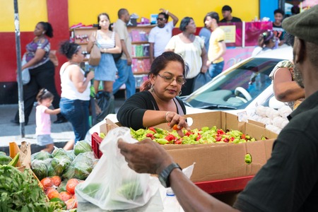 Port of spain, Trinidad and Tobago - November 28, 2015: old woman buys vegetables or fruit outdoors on local south market on streetscape backgroundのeditorial素材