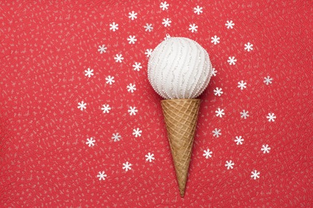 Christmas or New Year decorations with ice cream cone, white silver christmas ball and white decorative snowflakes arranged around on red texture backgroundの写真素材