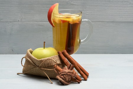 Glass of delicious glintwein or mulled hot wine with cinnamon placed inside and natural fresh green apple inside sack bag with string on vinage wooden backgroundの写真素材