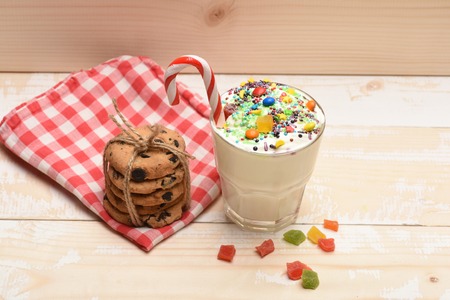 Glass of milk shake with cream, sprinkles, striped candy, colorful dragee inside, marmalade jelly...