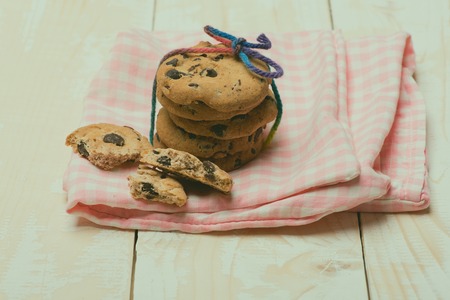 Chocolate chip cookies tied with rainbow string on checkered pink napkin on white wooden background, side viewの写真素材