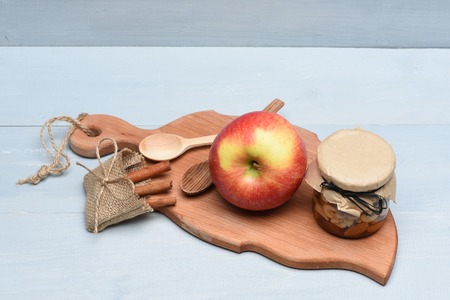 Fresh red apple and different types of nuts in glass jar, cinnamon in sack bag on cutting board with string and spoons on vintage wooden backgroundの写真素材