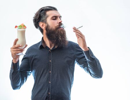 handsome bearded man with stylish hair mustache and beard on serious face holding glass of nonalcoholic beverage and smoking cigarette isolated on whiteの写真素材