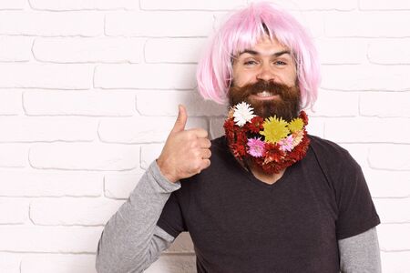 handsome bearded man with stylish mustache in pink wig with colorful autumn flowers in long beard on...