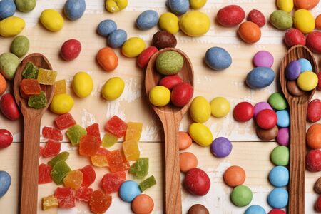 Mix of colorful dragee with raisins or peanuts inside, marmalade or jelly candies, wooden spoons on vintage wooden backgroundの写真素材
