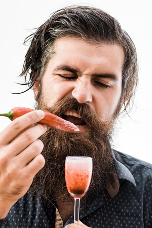 handsome bearded man with wet ruffled hair mustache and long beard on serious face holding glass of red alcoholic shot with chili and want taste it isolated on whiteの写真素材
