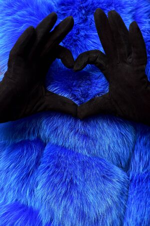 female hands in black fashionable velvet gloves make heart from fingers on colorful blue fur backgroundの写真素材