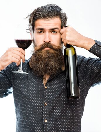 handsome bearded rich man with stylish hair mustache and long beard on serious face in blue fashion shirt holding glass of red wine and bottle isolated on whiteの写真素材
