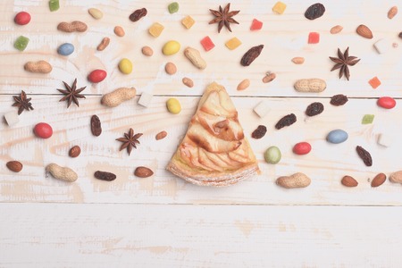 Single slice of apple pie with mix of colorful dragee, marmalade or jelly candies, almonds, peanuts, raisins, anise, sugar cubes on vintage wooden backgroundの写真素材