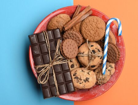 Oatmeal chocolate cookies, pastry, cinnamon, candy and dark chocolate bar with thread in red saucepan on colorful backgroundの写真素材