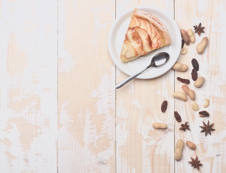 Single slice of apple pie with peanuts, raisins anise and white plate, spoon on vintage wooden backgroundの写真素材