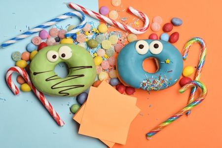 Green and blue funny glazed donuts with chocolate and sprinkles, striped caramel candies, colorful dragee with raisins or peanuts inside, marmalade or jelly candies on colorful background, copy spaceの写真素材