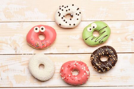 Colorful funny glazed donuts with coconut, icing or sprinkles, nuts and chocolate on vintage wooden backgroundの写真素材