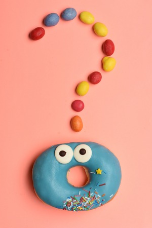 Blue funny surprised glazed donut with icing or sprinkles and colorful dragee with raisins or peanuts inside on pink backgroundの写真素材