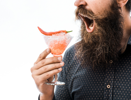 bearded man with lush beard holding glass of alcoholic cocktail with red chili and ice isolated on whiteの写真素材