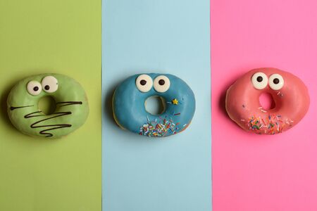 Colorful funny glazed donuts with icing or sprinkles and chocolate on colorful backgroundの写真素材