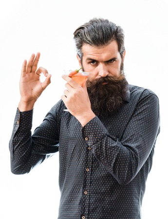 handsome bearded man with stylish hair mustache and long beard on serious face holding glass of alcoholic cocktail with red chili isolated on whiteの写真素材