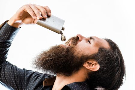 handsome bearded fashion man with stylish hair mustache and long beard on serious face drinking from metallic flask isolated on whiteの写真素材