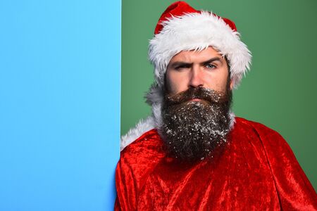 handsome bearded man with stylish mustache and long snowy beard on serious face in red santa suit on...
