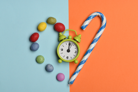 Green alarm clock with colorful dragee with raisins or peanuts inside and striped caramel candies on colorful backgroundの写真素材