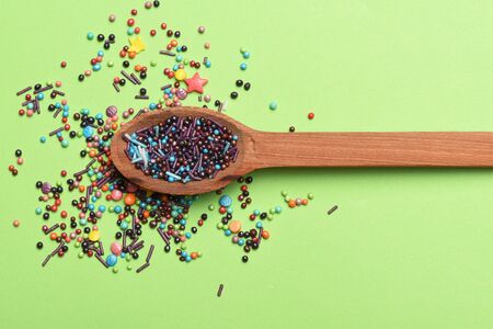 Colorful sugar sprinkles with wooden spoon on green background, decoration for cake and bakeryの写真素材