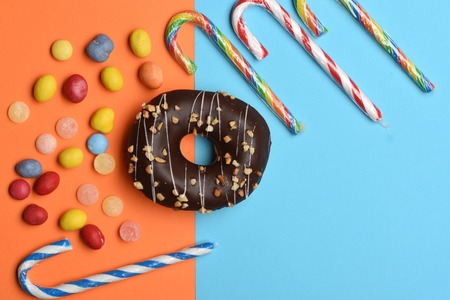 Chocolate glazed donut with nuts and colorful dragee with raisins or peanuts inside, marmalade or jelly candies, striped caramel candies on colorful backgroundの写真素材