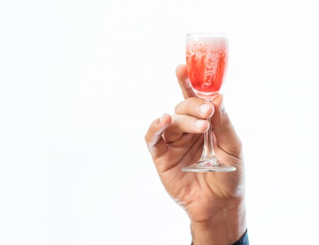 strong male hand carefully holding glass of red alcoholic beverage isolated on white