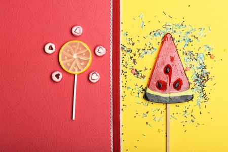 Set of lollipops as watermelon, lemon and candies with valentine heart sign, red ribbon and sprinkles on colorful background, top viewの写真素材
