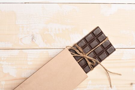 Dark chocolate bar with thread in crafted package on vintage wooden background