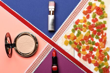Lipstick, cosmetic powder and mix of marmalade or jelly candies, and red ribbon on colorful background, children`s cosmeticの写真素材