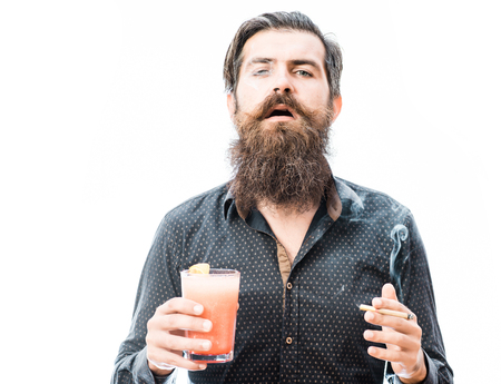 handsome bearded man with stylish hair mustache and long beard on serious face holding glass of nonalcoholic cocktail and smoking cigarette isolated on whiteの写真素材