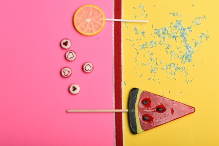 Set of lollipops as watermelon, lemon and candies with valentine heart sign, red ribbon and sprinkles on colorful background, top viewの写真素材