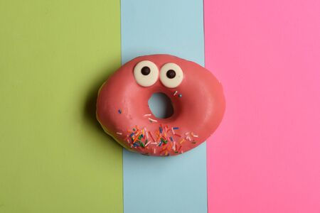 Pink funny surprised glazed donut with sprinkles on colorful background