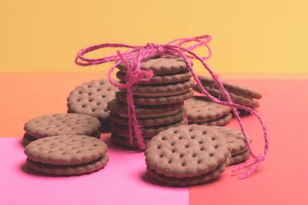 Chocolate chip cookies tied with pink string and placed around on colorful red yellow background, side viewの写真素材