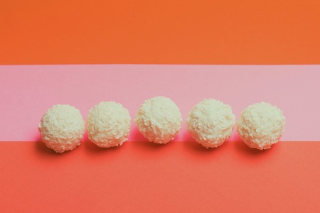 White chocolate coconut candies placed in row on colorful orange pink backgroundの写真素材