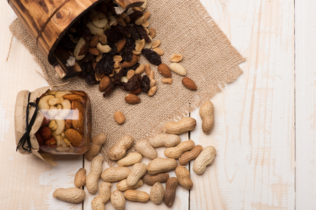 Different types of nuts in glass jar and poured from cask on sacking napkin on white wooden...