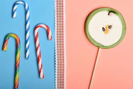 Set of striped caramel candies and lollipop as green apple with red ribbon on colorful backgroundの写真素材