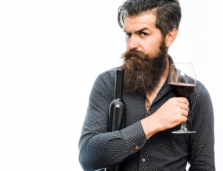 handsome bearded rich man with stylish hair mustache and long beard on serious face in blue fashion shirt holding glass of red wine and bottle isolated on white, copy spaceの写真素材