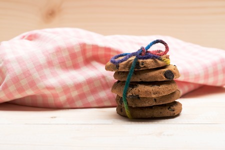 Chocolate chip cookies tied with rainbow string with checkered pink napkin on white wooden...