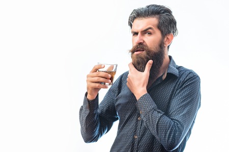 handsome bearded man with stylish hair mustache and long beard on serious face in blue fashion shirt holding glass of whiskey isolated on white, copy spaceの写真素材