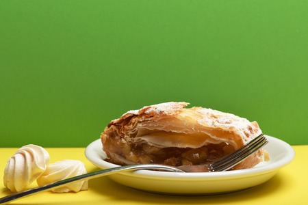 tasty apple strudel pie on white plate near white marshmallows and silver fork on colorful yellow and green background, copy spaceの写真素材