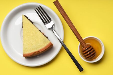 single slice of pie with poppy seeds on white plate near silver fork, honey and stick on yellow background, top viewの写真素材