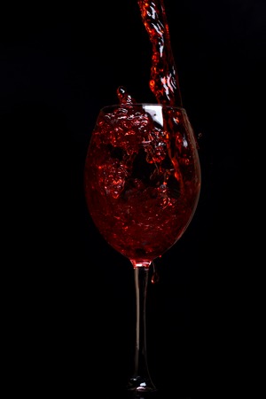 pouring glass with beautiful stream and dropse of red wine on black background, side viewの写真素材